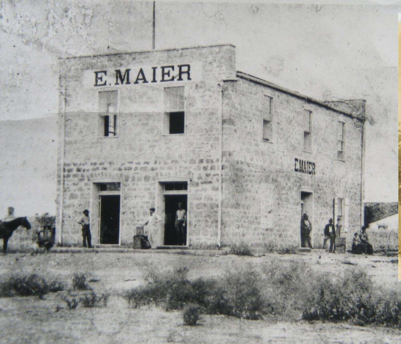 Early photo of the two-story limestone E. Maier store in Fredericksburg, Texas, with the name painted on the front and side and no porch