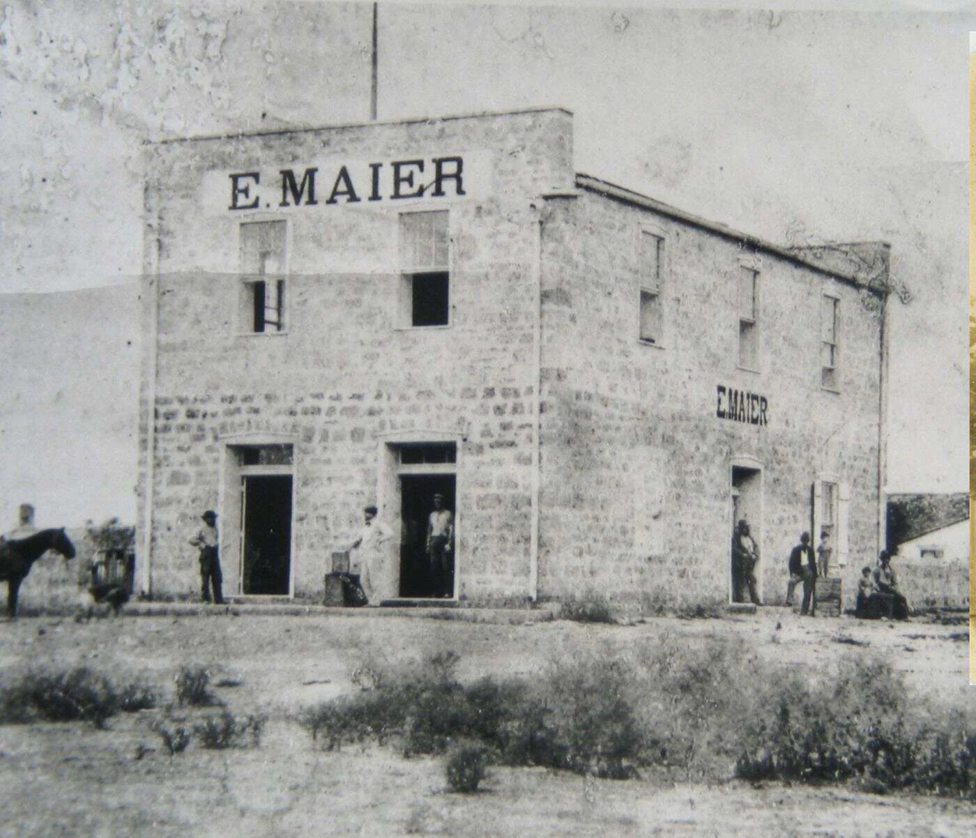 Early photo of the two-story limestone E. Maier store in Fredericksburg, Texas, with the name painted on the front and side and no porch