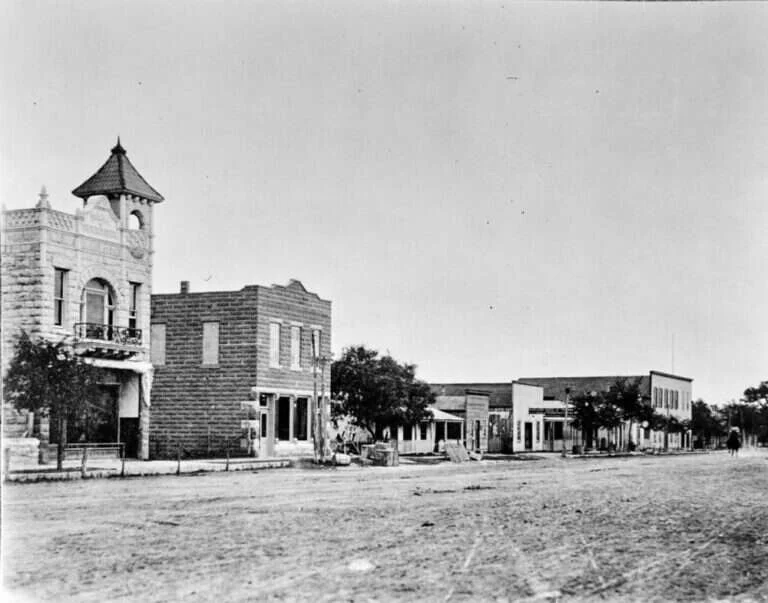 Dirt Main Street in Fredericksburg, Texas, in 1905, lined with stone storefronts