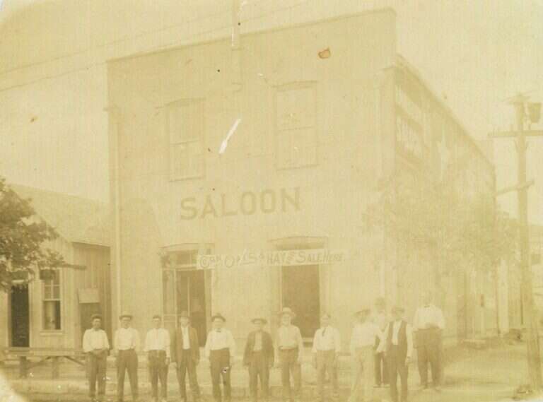 Men lined up in front of the Maier Building in Fredericksburg, Texas, with SALOON painted across the limestone front