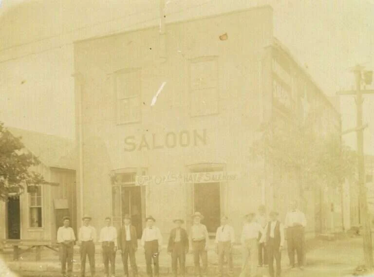 Men lined up in front of the Maier Building in Fredericksburg, Texas, with SALOON painted across the limestone front