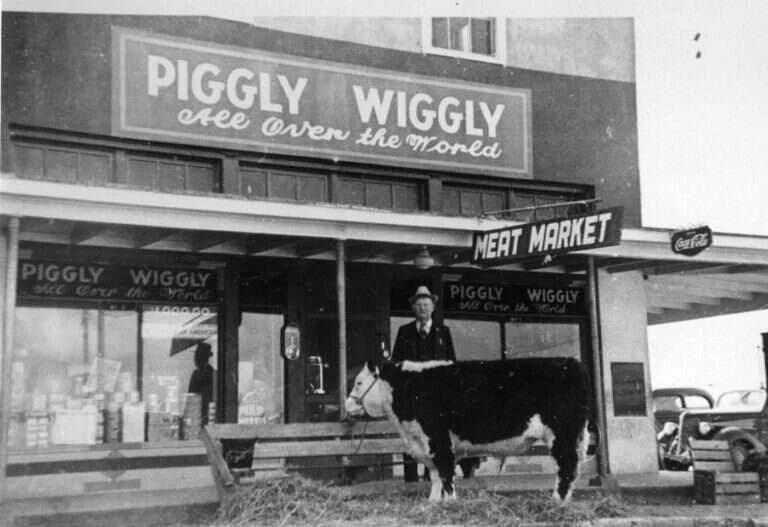 Piggly Wiggly grocery and meat market storefront at the Maier Building in Fredericksburg, Texas, with a man and a steer out front