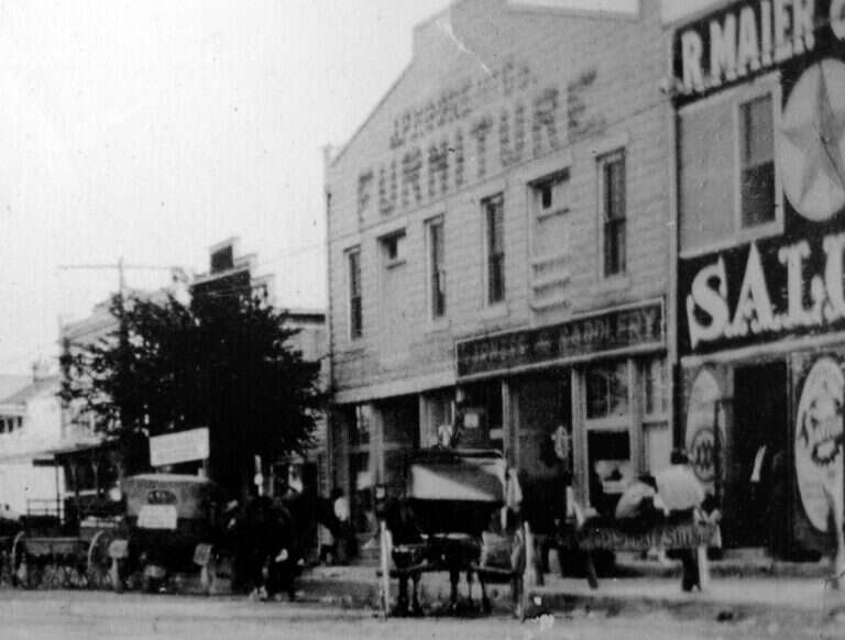 Historic photo of Main Street in Fredericksburg with horse-drawn wagons outside the R. Maier saloon at 101 E. Main