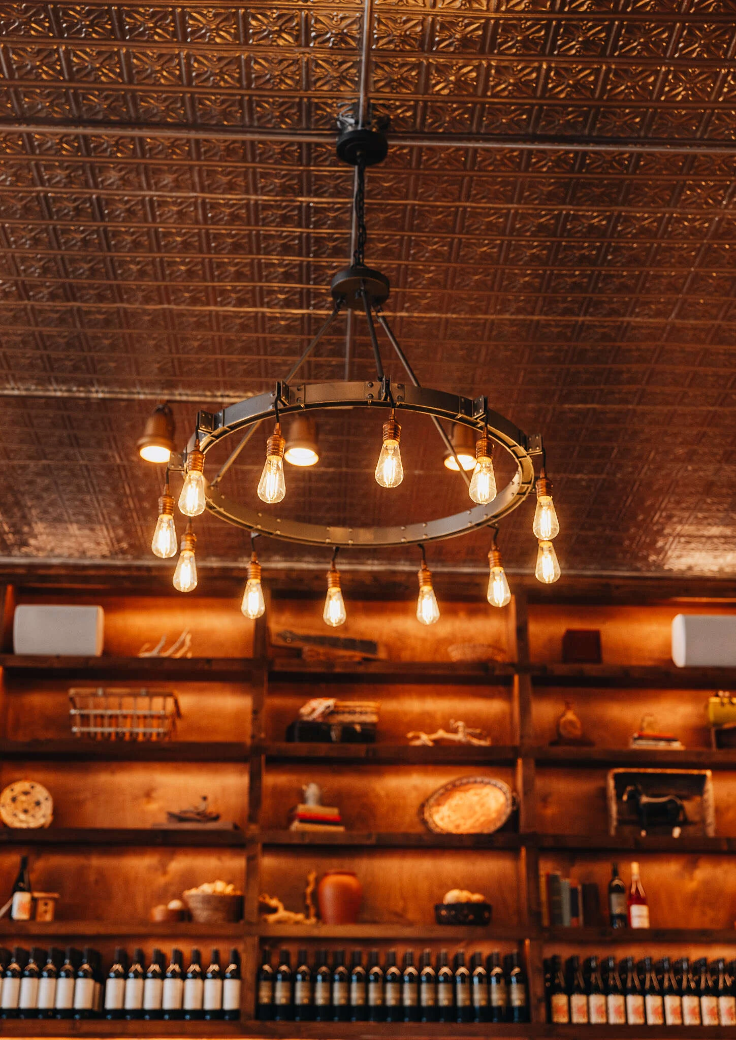 Edison-bulb chandelier under the pressed tin ceiling at William Chris Fredericksburg, with lit shelves of William Chris wine below